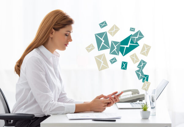 Side view of businesswoman using smartphone near documents and laptop on table, e-mail illustration